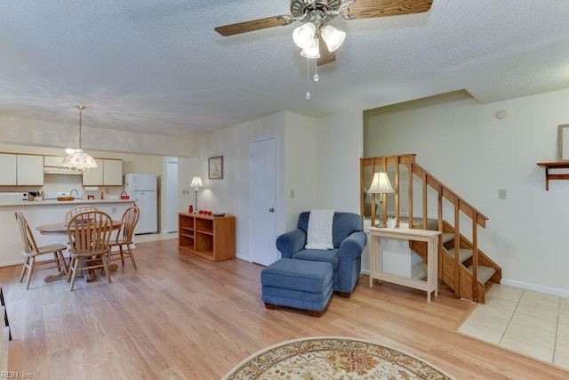 living room featuring ceiling fan with notable chandelier, a textured ceiling, and light hardwood / wood-style floors