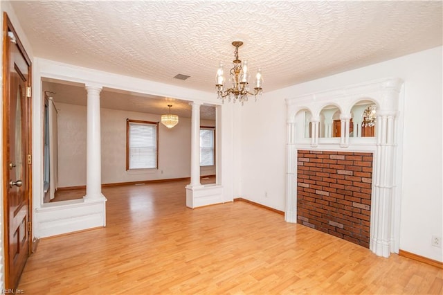 unfurnished living room featuring decorative columns, hardwood / wood-style floors, and a textured ceiling