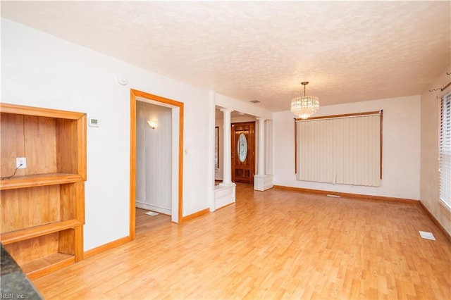 empty room featuring a chandelier, decorative columns, light hardwood / wood-style flooring, and a textured ceiling