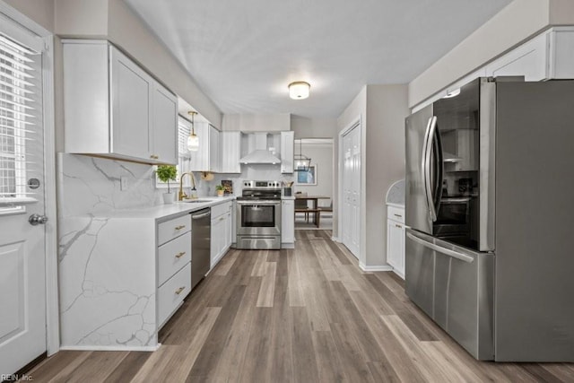 kitchen featuring wall chimney exhaust hood, sink, light hardwood / wood-style flooring, appliances with stainless steel finishes, and white cabinets