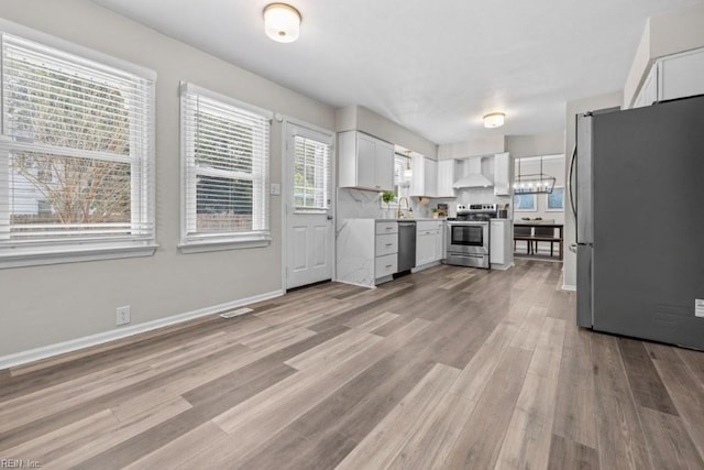 kitchen with light hardwood / wood-style flooring, wall chimney range hood, white cabinets, stainless steel appliances, and backsplash