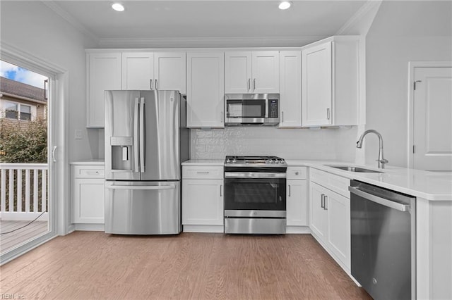 kitchen with sink, light wood-type flooring, ornamental molding, stainless steel appliances, and white cabinets