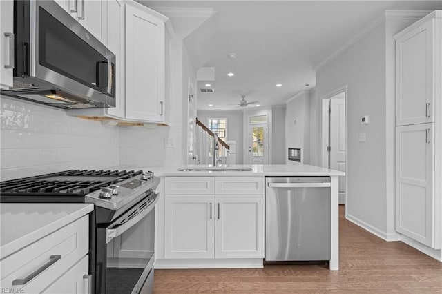 kitchen featuring crown molding, appliances with stainless steel finishes, white cabinetry, kitchen peninsula, and light wood-type flooring