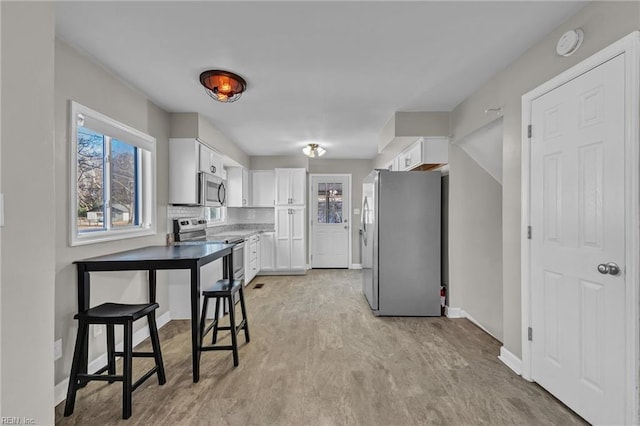 kitchen with white cabinetry, stainless steel appliances, light hardwood / wood-style floors, and tasteful backsplash