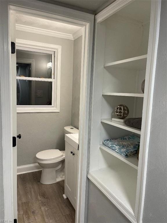 bathroom featuring wood-type flooring, ornamental molding, vanity, and toilet