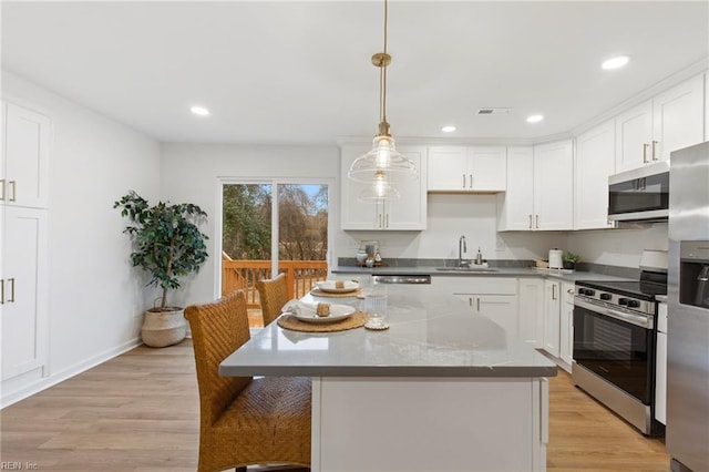 kitchen with sink, a center island, hanging light fixtures, stainless steel appliances, and white cabinets