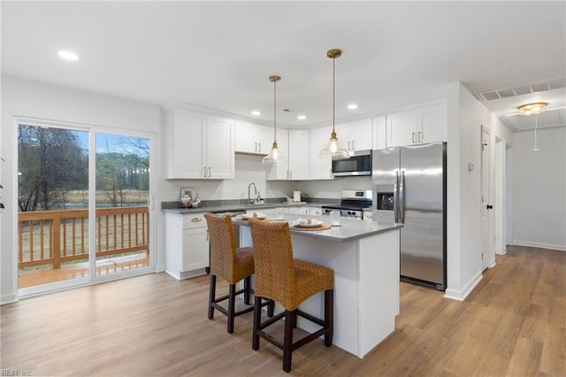 kitchen with appliances with stainless steel finishes, white cabinetry, hanging light fixtures, a kitchen breakfast bar, and a kitchen island