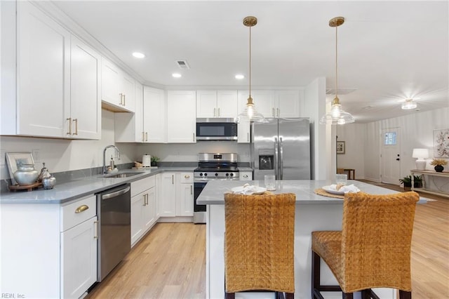 kitchen with a kitchen bar, sink, white cabinetry, pendant lighting, and stainless steel appliances