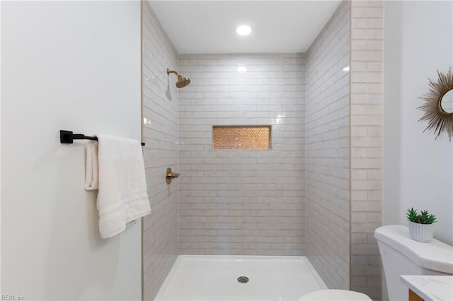 bathroom featuring vanity, a tile shower, and toilet