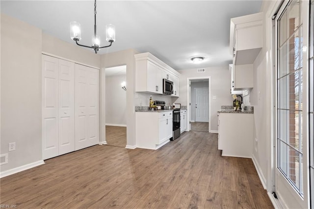 kitchen with appliances with stainless steel finishes, hardwood / wood-style floors, white cabinets, and decorative light fixtures