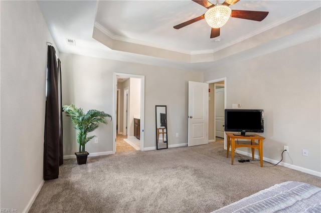 carpeted bedroom with a raised ceiling, ornamental molding, ceiling fan, and ensuite bath