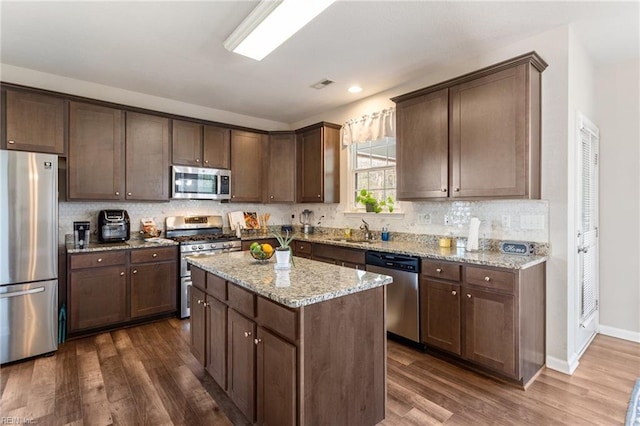 kitchen featuring dark wood-type flooring, light stone counters, a kitchen island, stainless steel appliances, and decorative backsplash