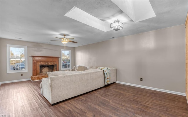 living room featuring ceiling fan, a fireplace, dark hardwood / wood-style floors, and a skylight