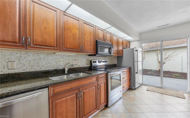 kitchen featuring sink, light tile patterned floors, dark stone countertops, stainless steel appliances, and backsplash