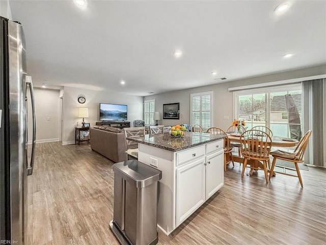 kitchen featuring stainless steel refrigerator, white cabinets, a kitchen island, dark stone counters, and light wood-type flooring