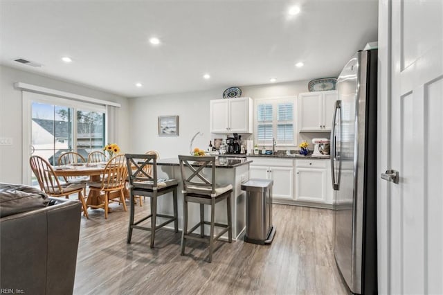 kitchen with stainless steel fridge, a kitchen breakfast bar, a kitchen island with sink, and white cabinets