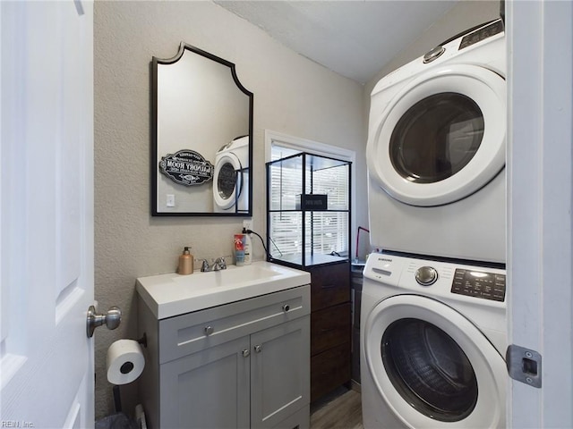 laundry area with cabinets, stacked washing maching and dryer, sink, and dark wood-type flooring