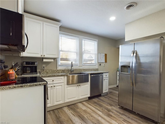 kitchen with sink, white cabinetry, light wood-type flooring, appliances with stainless steel finishes, and stone counters