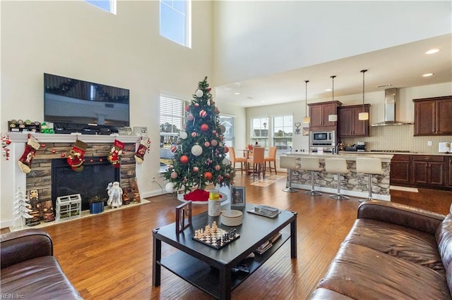 living room featuring hardwood / wood-style flooring, a stone fireplace, and a high ceiling