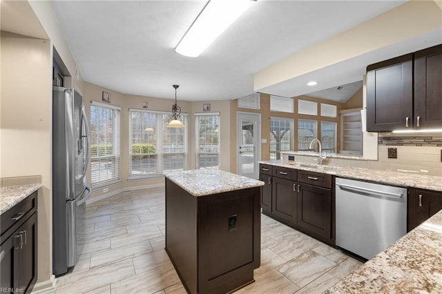 kitchen featuring stainless steel appliances, a kitchen island, light stone countertops, and dark brown cabinets