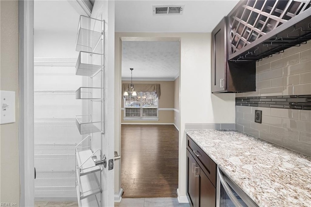 kitchen with dark brown cabinetry, a notable chandelier, pendant lighting, light stone countertops, and decorative backsplash