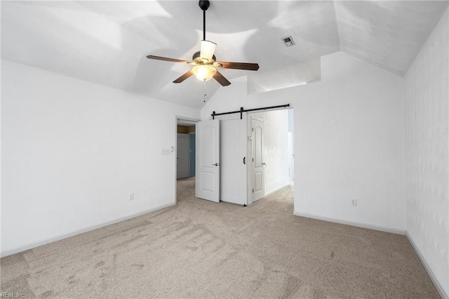 unfurnished bedroom featuring vaulted ceiling, a barn door, light colored carpet, and ceiling fan