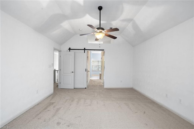 interior space with vaulted ceiling, a barn door, light carpet, and ceiling fan