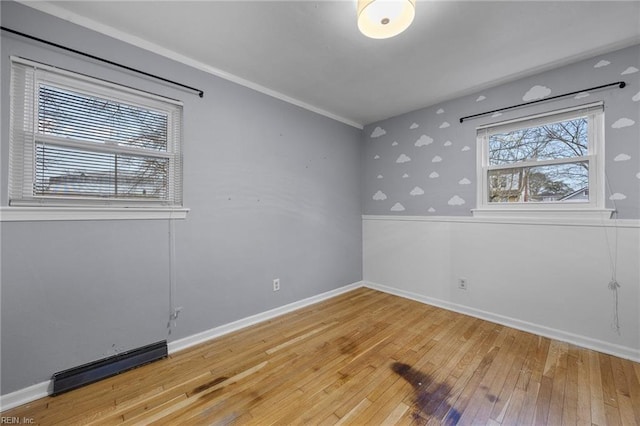 empty room with crown molding, wood-type flooring, and a baseboard heating unit