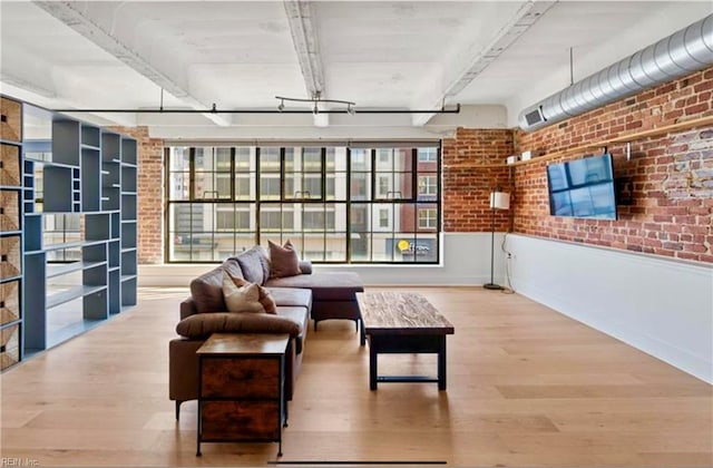 living area with brick wall, wainscoting, and wood finished floors