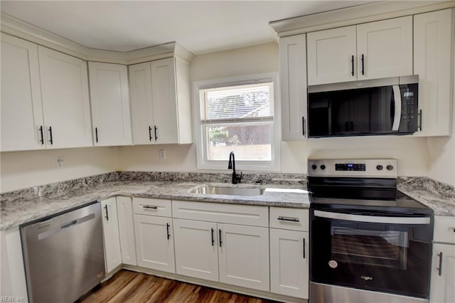 kitchen with appliances with stainless steel finishes, white cabinetry, sink, light stone counters, and light wood-type flooring