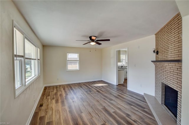 unfurnished living room with ceiling fan, a fireplace, sink, and wood-type flooring