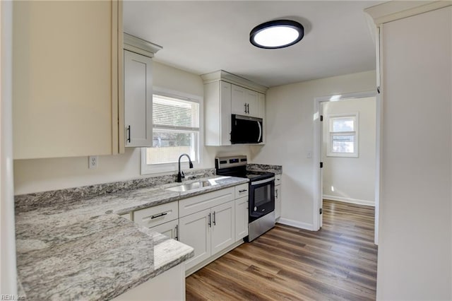 kitchen featuring a wealth of natural light, sink, stainless steel appliances, light stone countertops, and dark wood-type flooring