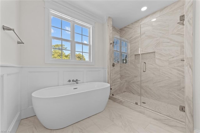 bathroom featuring marble finish floor, wainscoting, a soaking tub, and a decorative wall