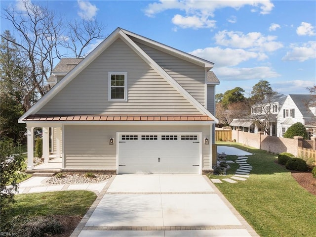 view of front of house with concrete driveway, a standing seam roof, covered porch, fence, and a front yard