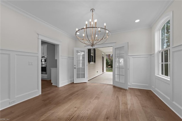 unfurnished dining area with wood finished floors, an inviting chandelier, crown molding, french doors, and a decorative wall