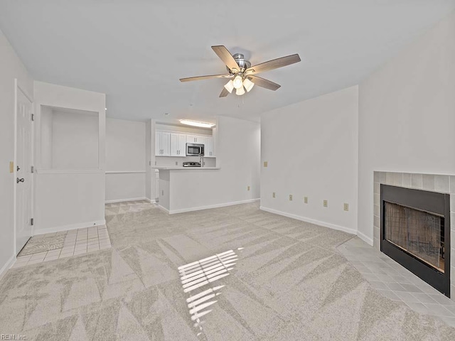 unfurnished living room with light colored carpet, a fireplace, baseboards, and a ceiling fan