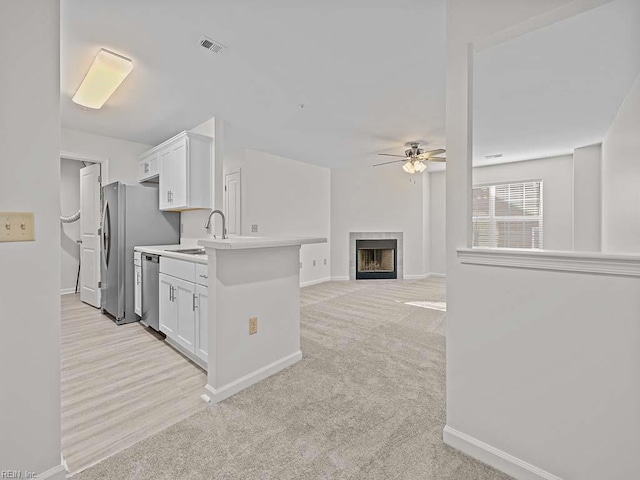 kitchen featuring visible vents, a ceiling fan, stainless steel dishwasher, white cabinetry, and light colored carpet