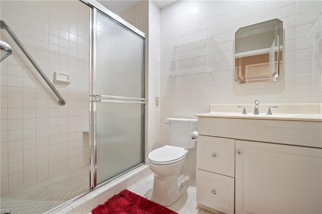 bathroom with a shower with door, tile walls, vanity, tile patterned floors, and toilet