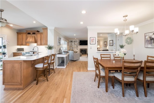 dining room featuring ornamental molding, sink, ceiling fan with notable chandelier, and light wood-type flooring