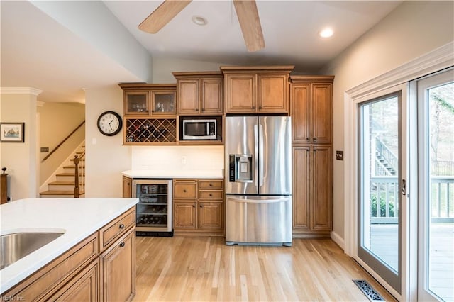 kitchen featuring appliances with stainless steel finishes, backsplash, wine cooler, ceiling fan, and light wood-type flooring