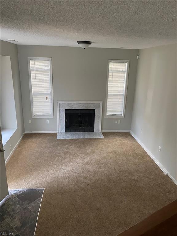 unfurnished living room with carpet flooring, a fireplace, a textured ceiling, and plenty of natural light