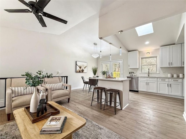 living room with sink, lofted ceiling with skylight, light hardwood / wood-style floors, and ceiling fan