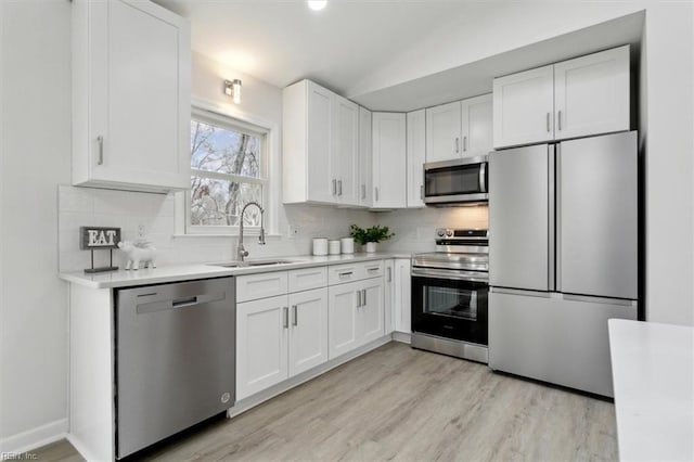 kitchen with tasteful backsplash, sink, white cabinets, stainless steel appliances, and light wood-type flooring