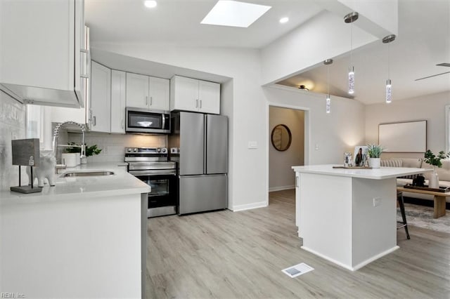 kitchen with appliances with stainless steel finishes, decorative light fixtures, sink, white cabinets, and a kitchen breakfast bar