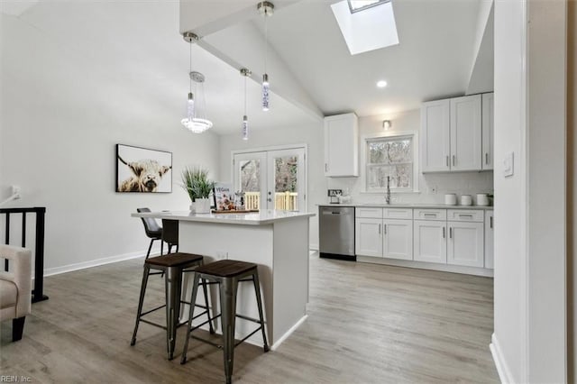 kitchen featuring lofted ceiling with skylight, a center island, hanging light fixtures, dishwasher, and white cabinets