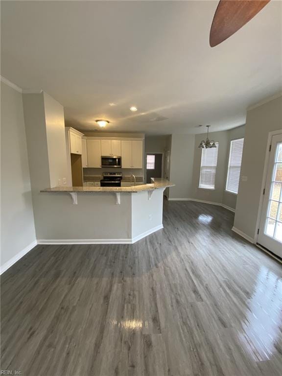 kitchen with appliances with stainless steel finishes, white cabinetry, a breakfast bar area, dark hardwood / wood-style flooring, and kitchen peninsula