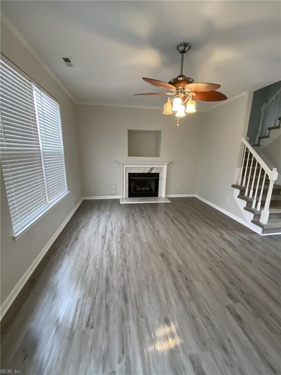 unfurnished living room with a premium fireplace, dark hardwood / wood-style floors, ceiling fan, and crown molding