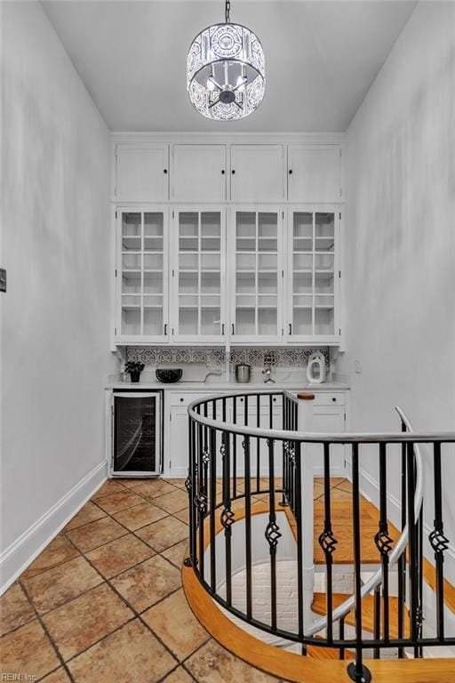 interior space with decorative light fixtures, white cabinetry, wine cooler, a chandelier, and decorative backsplash