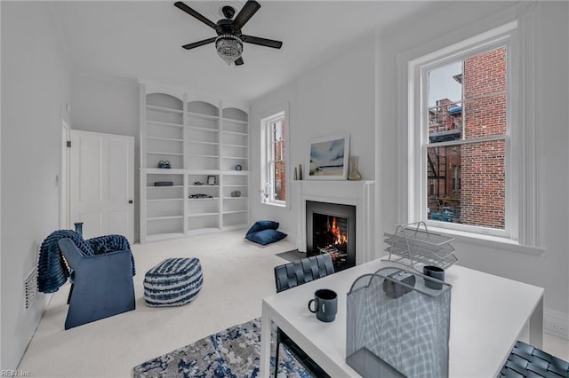 living room featuring built in shelves, ceiling fan, and carpet