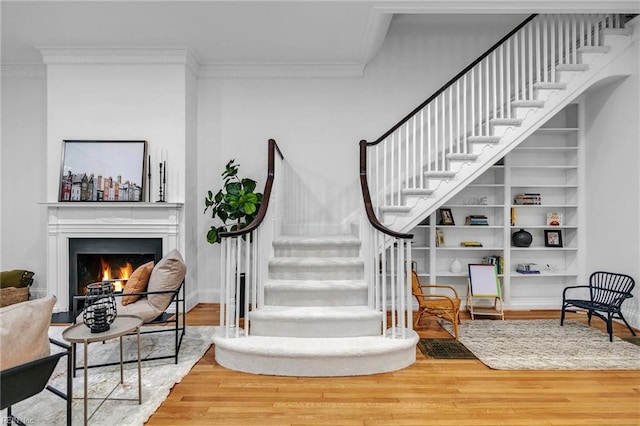 staircase with hardwood / wood-style floors, built in shelves, and ornamental molding